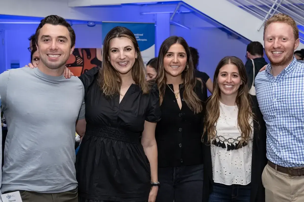 Young adult jewish life boston: Five young adults smile together at a social networking and community engagement event hosted indoors.