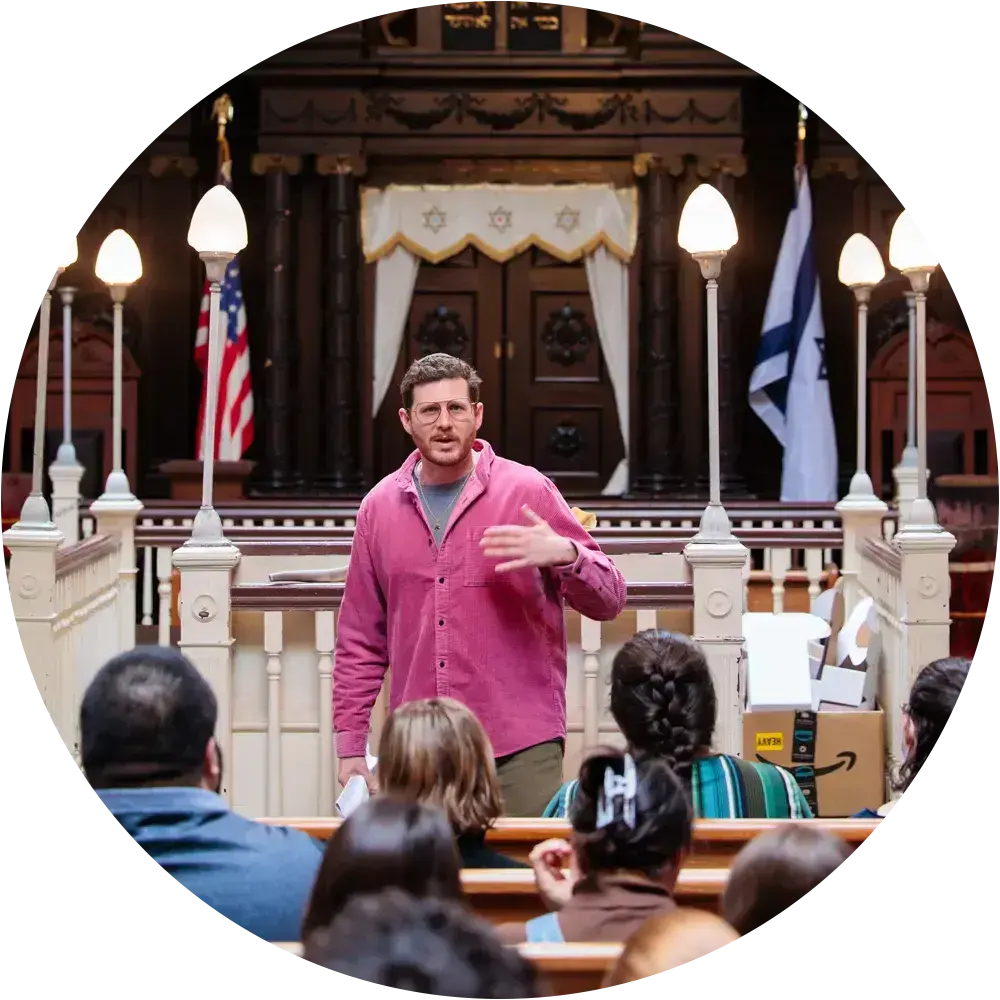 A man speaking to a congregation at a synagogue during an Acharai Leadership Program event.