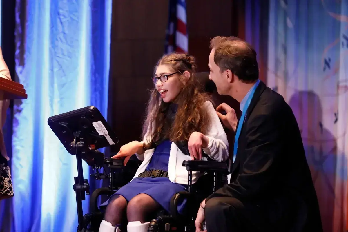 Smiling girl in a wheelchair on stage, enjoying a Jewish family event and activities for children in Boston.